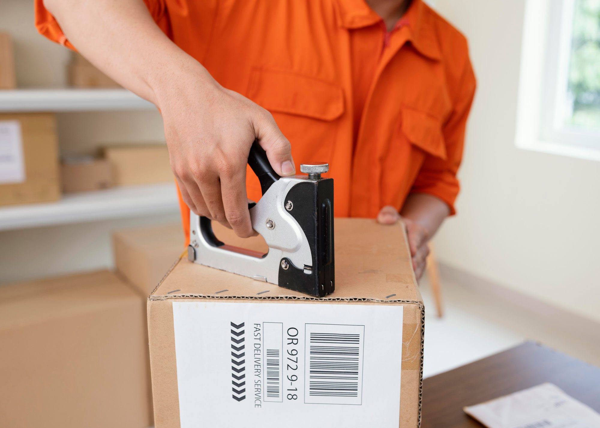 Man in an orange button-up shirt preparing a box for shipment